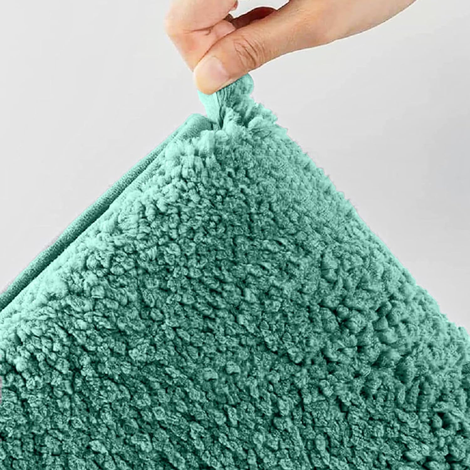 Hand holding a teal sherpa bathmat, soft textured bathroom accessory on white background