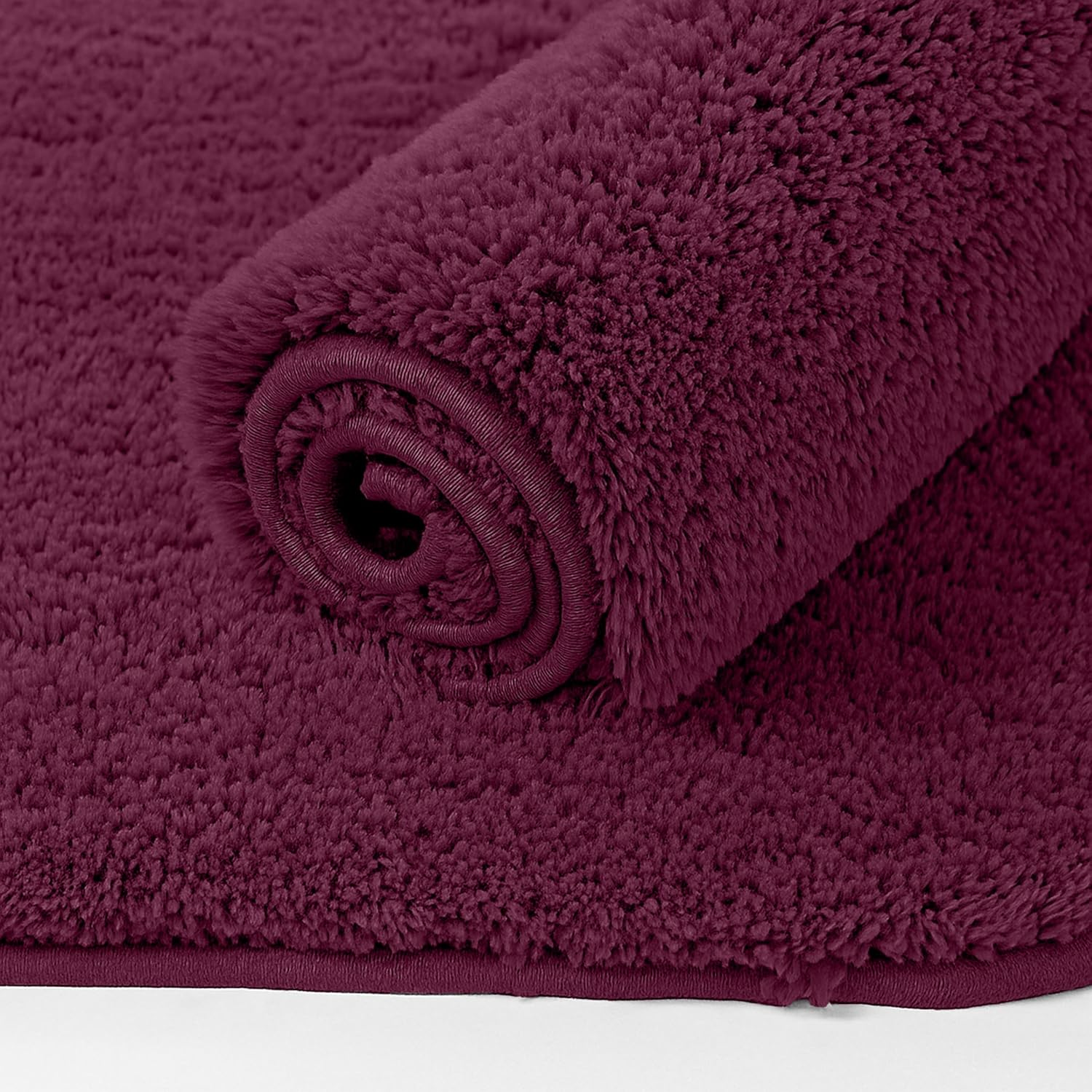 Plush maroon bathmat rolled up, soft texture, perfect for bathroom decor