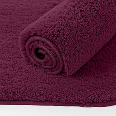 Plush maroon bathmat rolled up, soft texture, perfect for bathroom decor