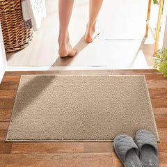 Beige bathmat on wooden floor near doorway with slippers and bare feet stepping out