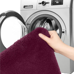 Hand holding a soft burgundy bathmat in front of a washing machine