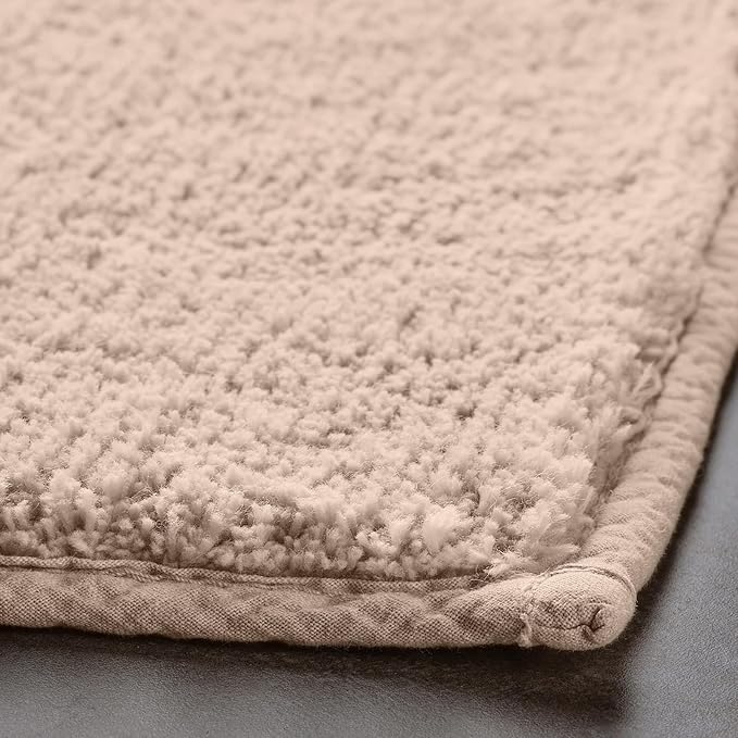 Beige textured bathmat with soft, plush surface and stitched border, close-up view