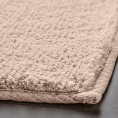 Beige textured bathmat with soft, plush surface and stitched border, close-up view
