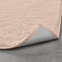 Beige bathmat with textured surface and non-slip backing on a grey floor