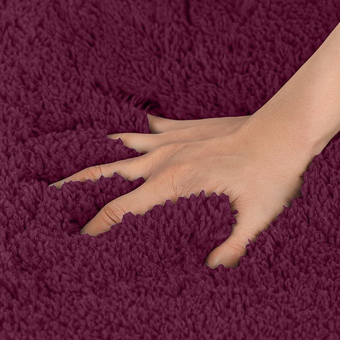 Hand pressing into a soft, plush maroon bathmat with thick, textured fibers