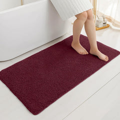 Plush maroon bathmat on white bathroom floor next to bathtub with person stepping on it