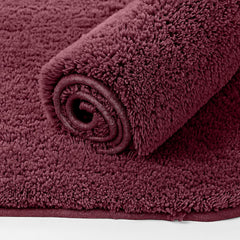 Soft maroon bathmat with plush textured surface, partially rolled on a white background