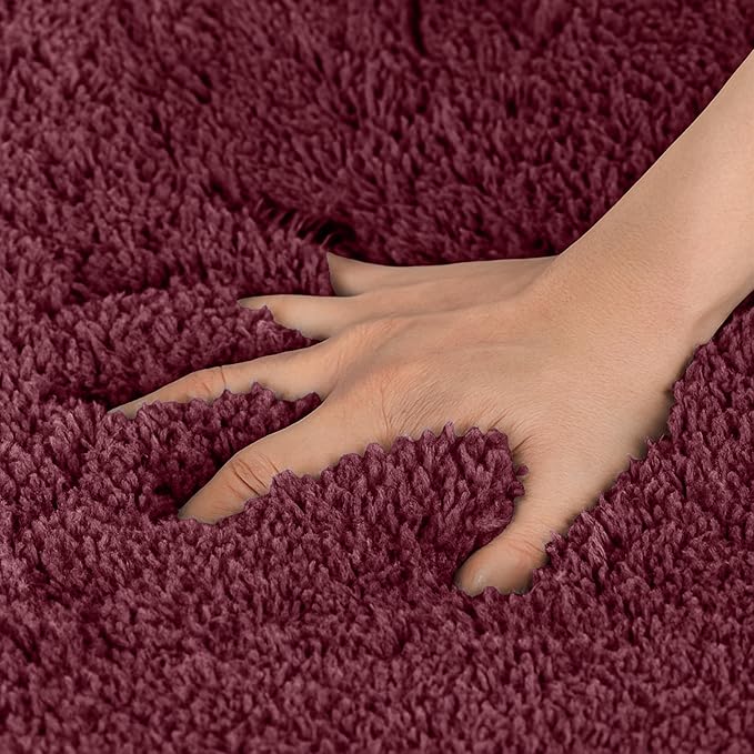 Hand pressing into soft burgundy bathmat, showing plush absorbent texture