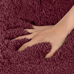 Hand pressing into soft burgundy bathmat, showing plush absorbent texture