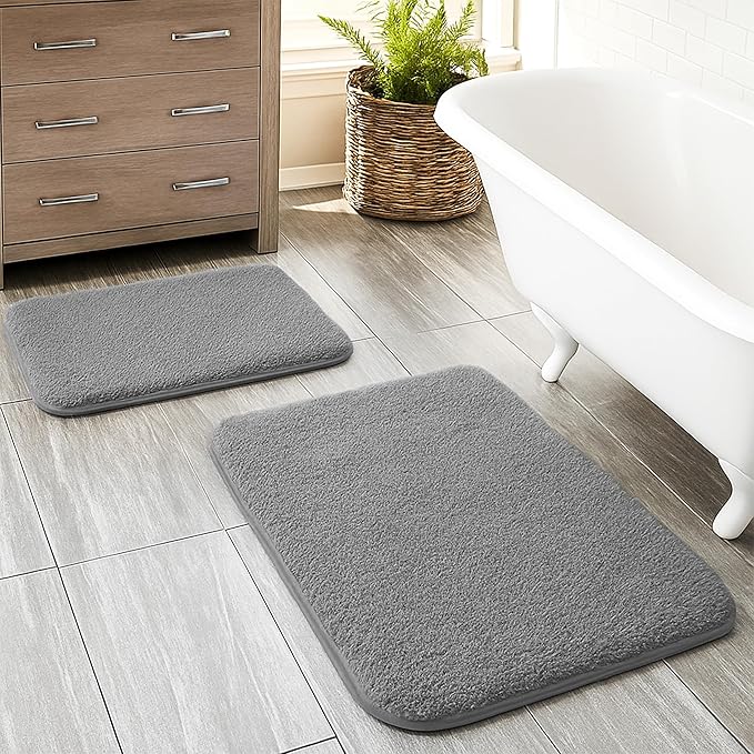 Two gray bathmats on a tiled bathroom floor near a bathtub and wooden cabinet
