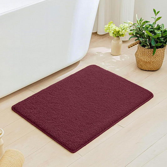 Plush maroon bathmat on light wood bathroom floor near bathtub and potted plants