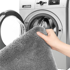 Hand holding a soft grey bathmat near a washing machine, showing washable home textile