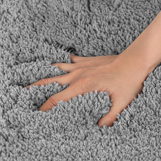 Hand pressing into soft, plush grey bathmat showing thick, absorbent texture