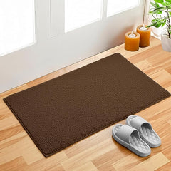 Brown bathmat on wooden floor by door with slippers, candles, and potted plant