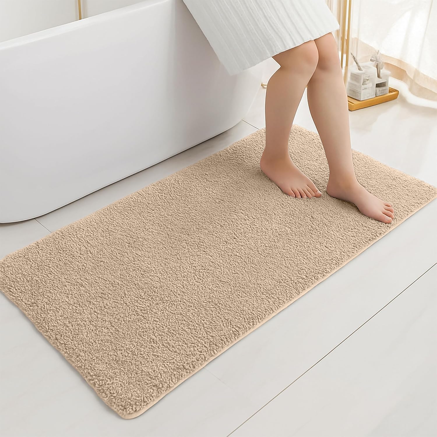 Beige bathmat on bathroom floor with person standing near white bathtub