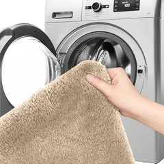 Hand holding a beige bathmat in front of an open washing machine