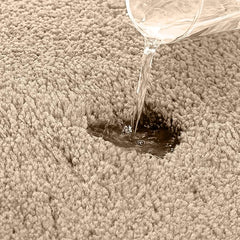 Water being poured onto a beige, absorbent bathmat to show its water resistance