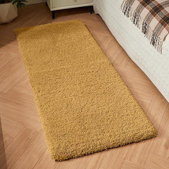 Soft yellow bathmat or bedroom runner rug on wooden floor beside a bed